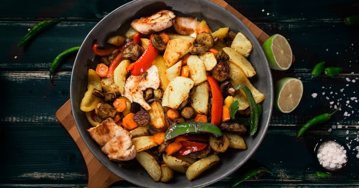 a pan filled with meat and vegetables on top of a wooden cutting board